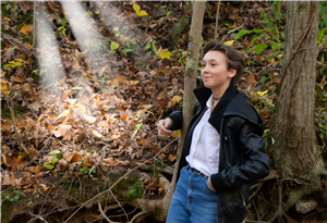student poses for a portrait in a jacket, holding a tree